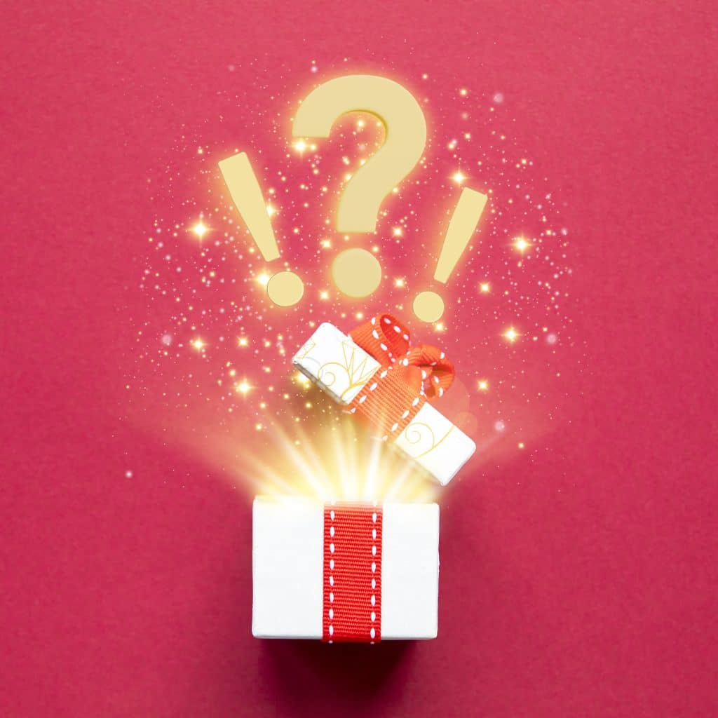 Une boîte cadeau ouverte d'où jaillissent des points d'exclamation et d'interrogation entourés de lumière scintillante sur un fond rouge, symbolisant des surprises et des découvertes inattendues