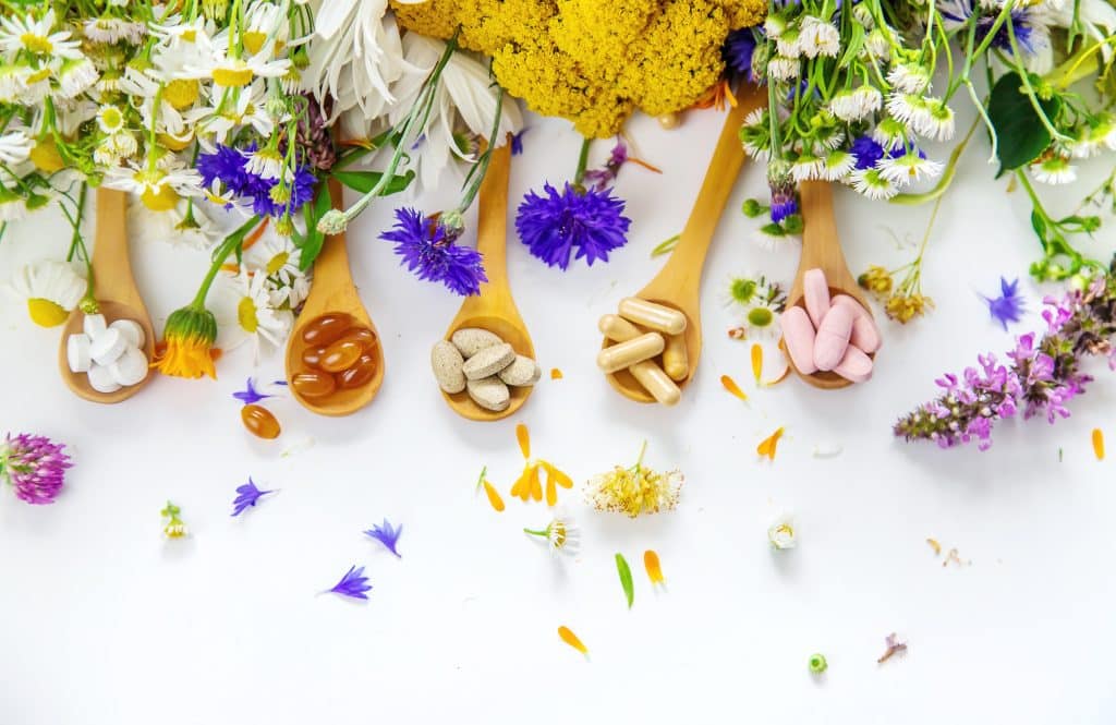 "Compléments alimentaires naturels présentés sur des cuillères en bois entourées de fleurs colorées