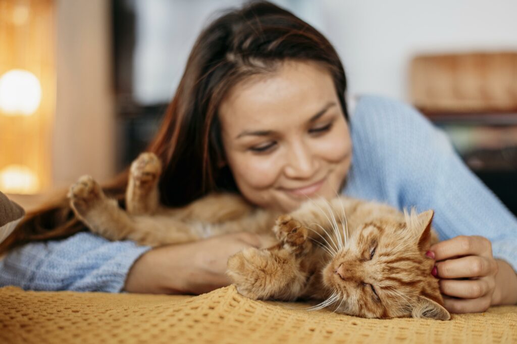 Une femme souriante caressant un chat roux allongé sur une couverture jaune